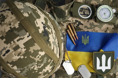 Photo of MYKOLAIV, UKRAINE - SEPTEMBER 26, 2020: Tactical gear and Ukrainian flag on camouflage background, flat lay