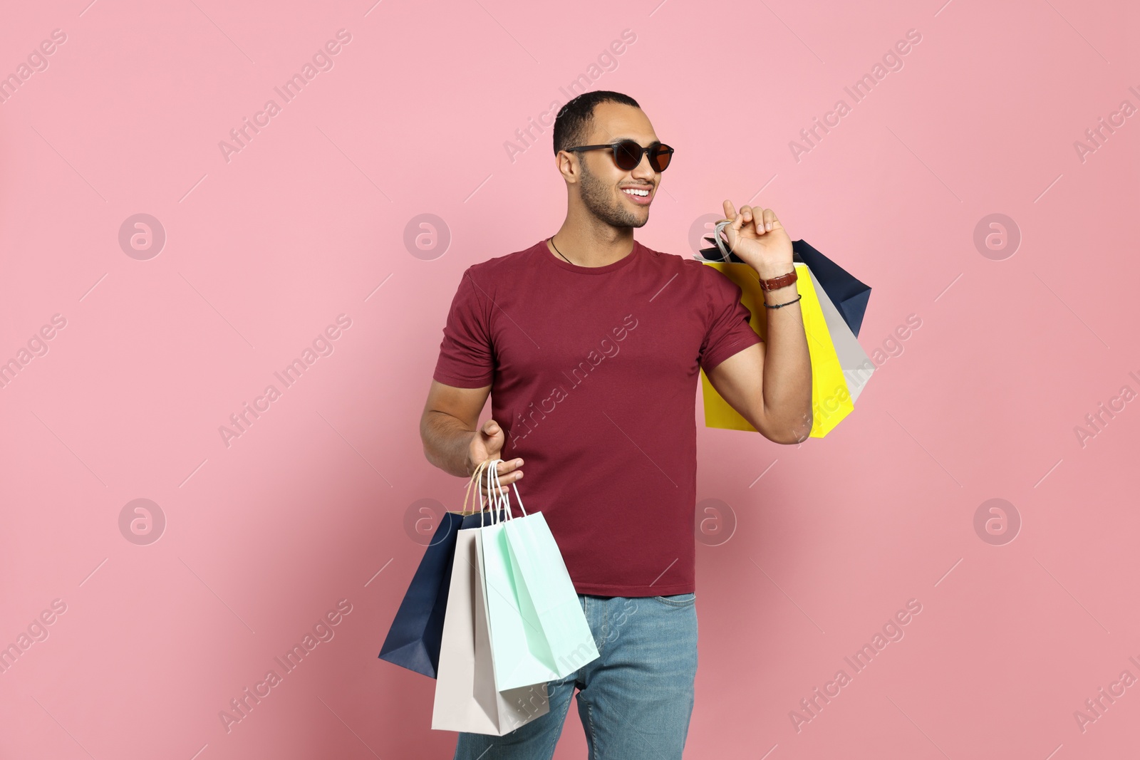 Photo of Happy African American man in sunglasses with shopping bags on pink background