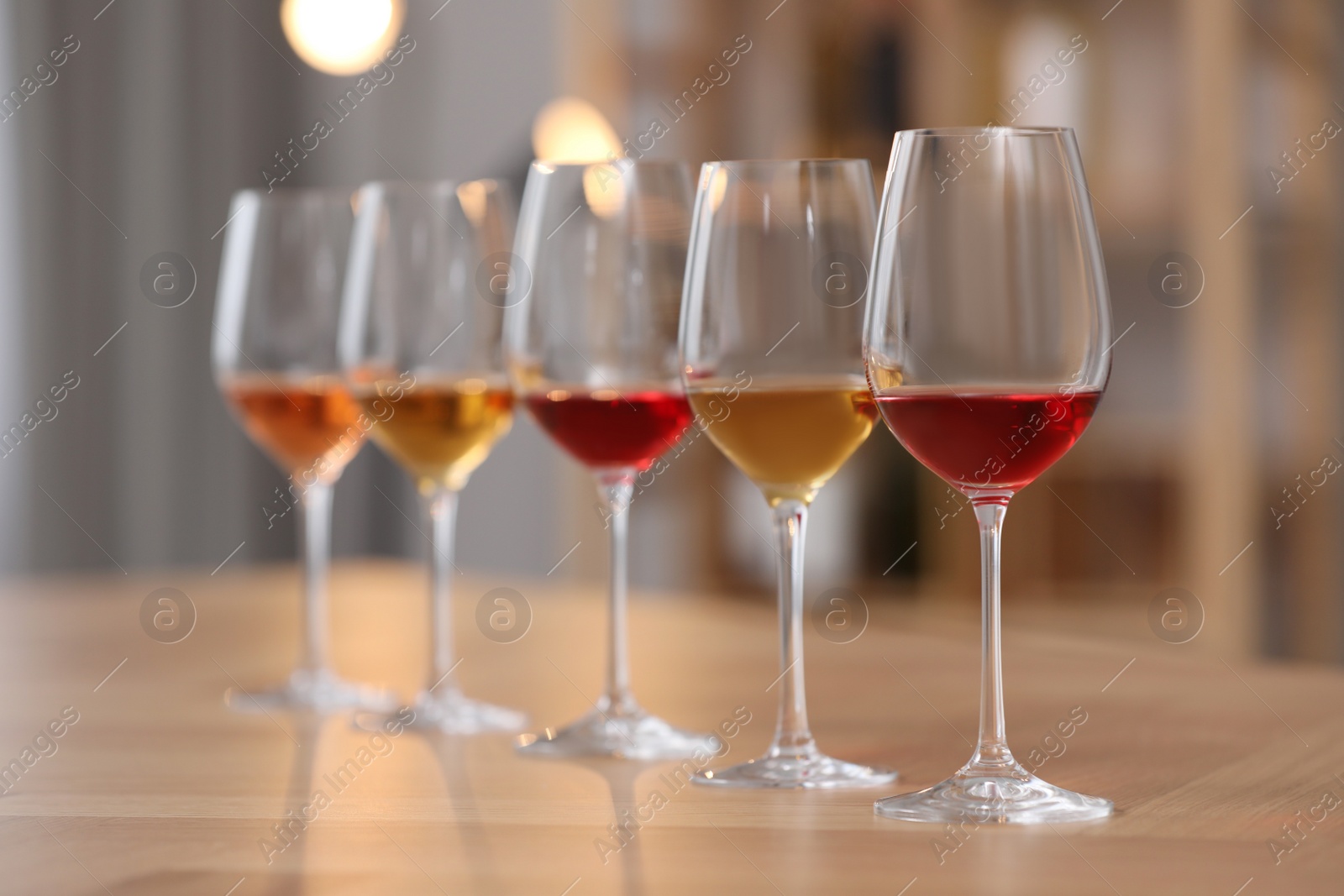 Photo of Different sorts of wine in glasses prepared for tasting on wooden table indoors