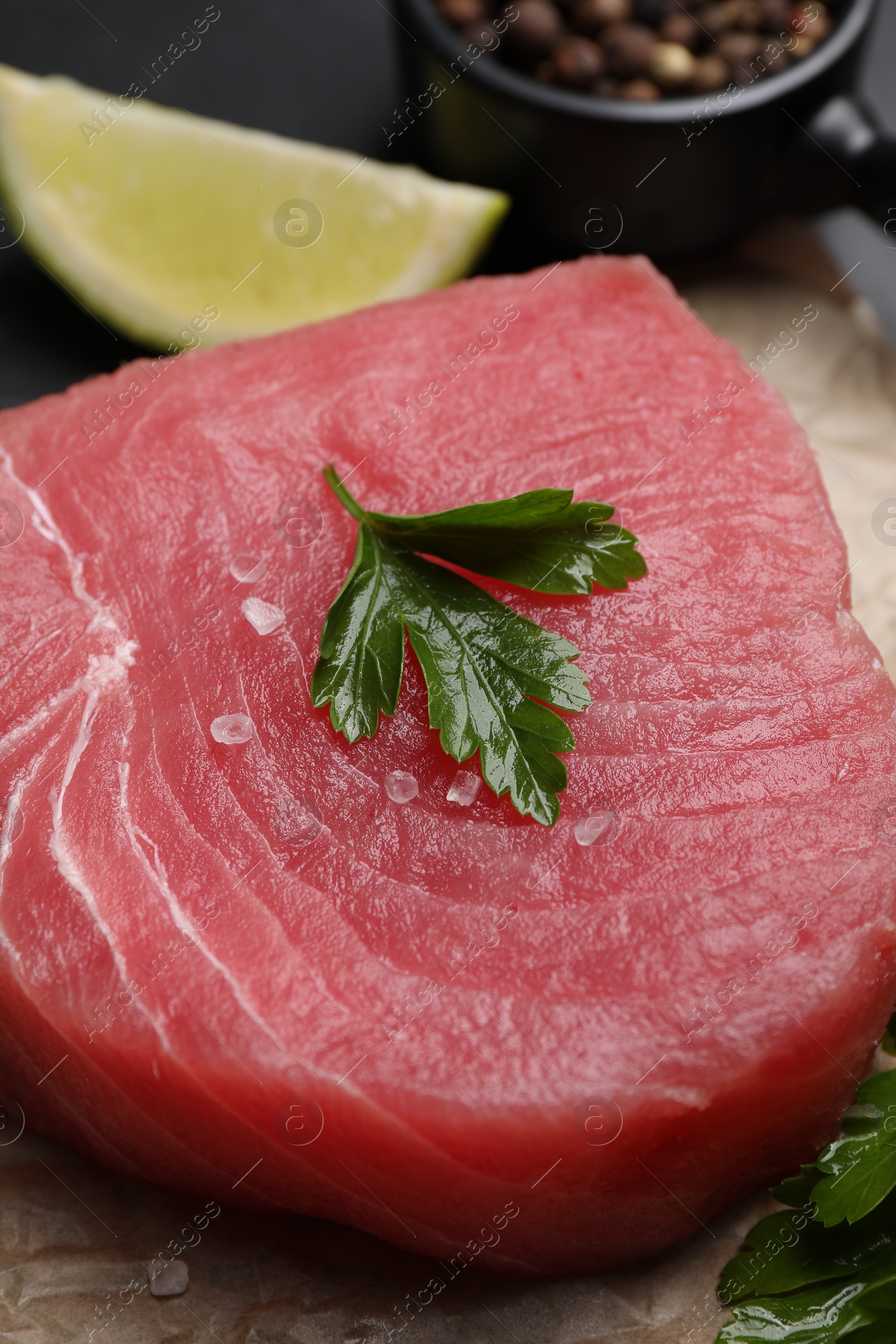 Photo of Raw tuna fillet with parsley and spices on table, closeup