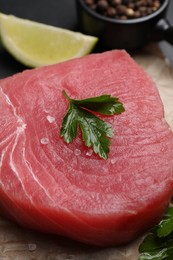 Raw tuna fillet with parsley and spices on table, closeup