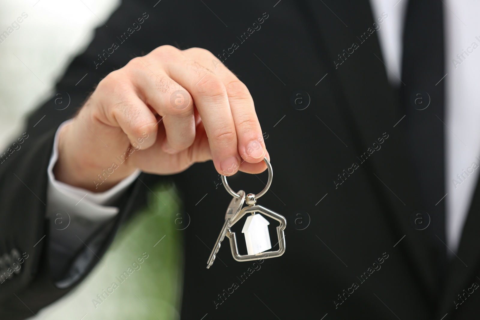 Photo of Real estate agent holding house key with trinket on blurred background, closeup