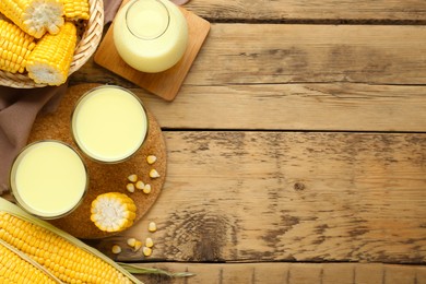 Photo of Tasty fresh corn milk in glasses and cobs on wooden table, flat lay. Space for text