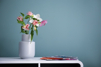 Photo of Vase with beautiful flowers on table against color background. Interior decor element