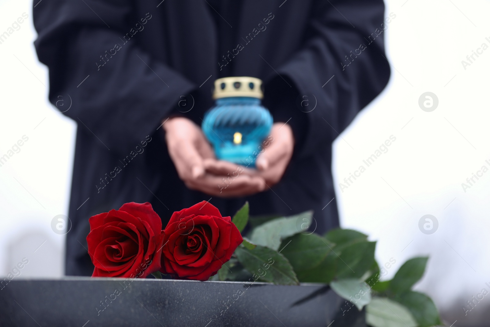 Photo of Woman with candle outdoors, focus on red roses. Funeral ceremony
