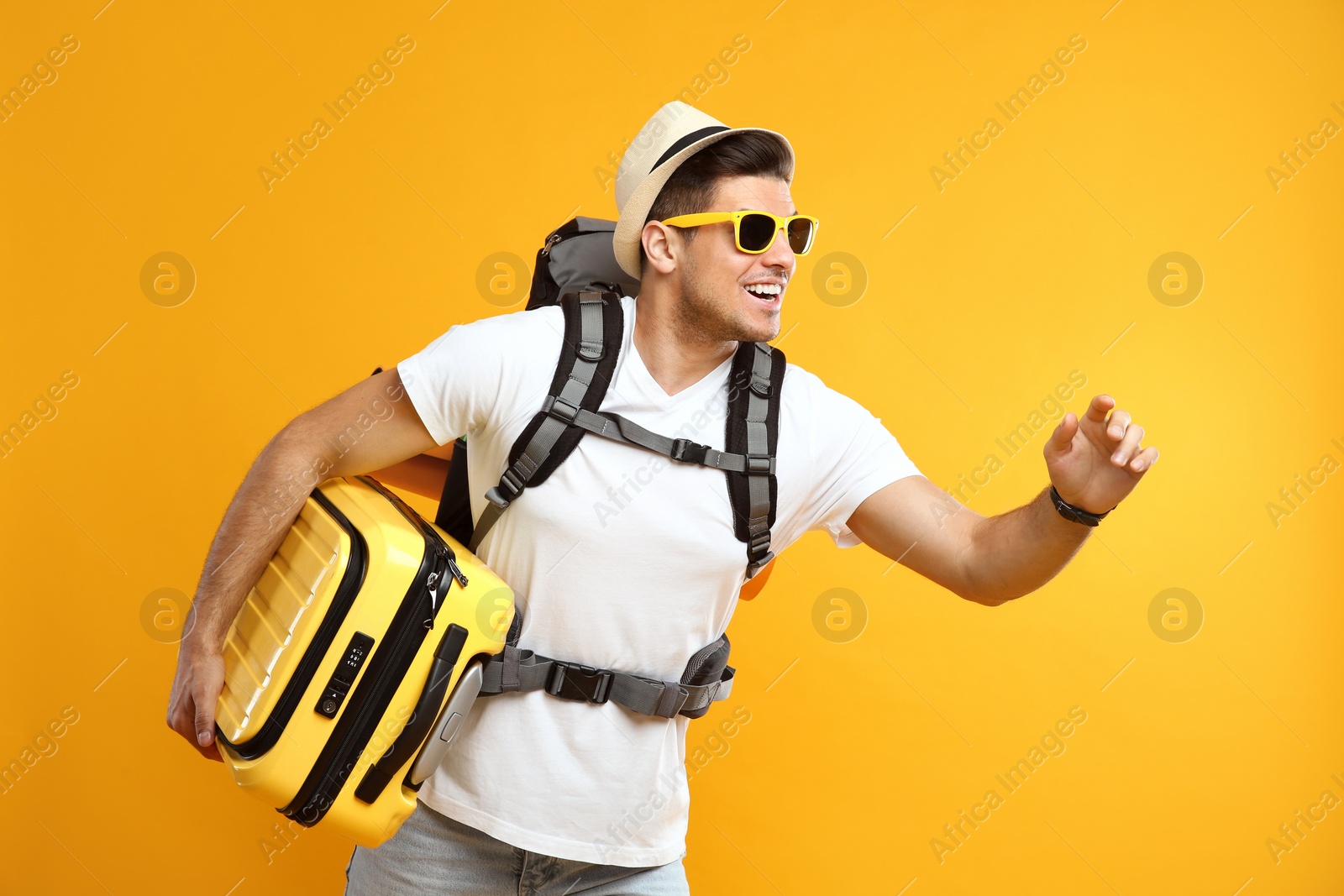 Photo of Male tourist with travel backpack and suitcase on yellow background