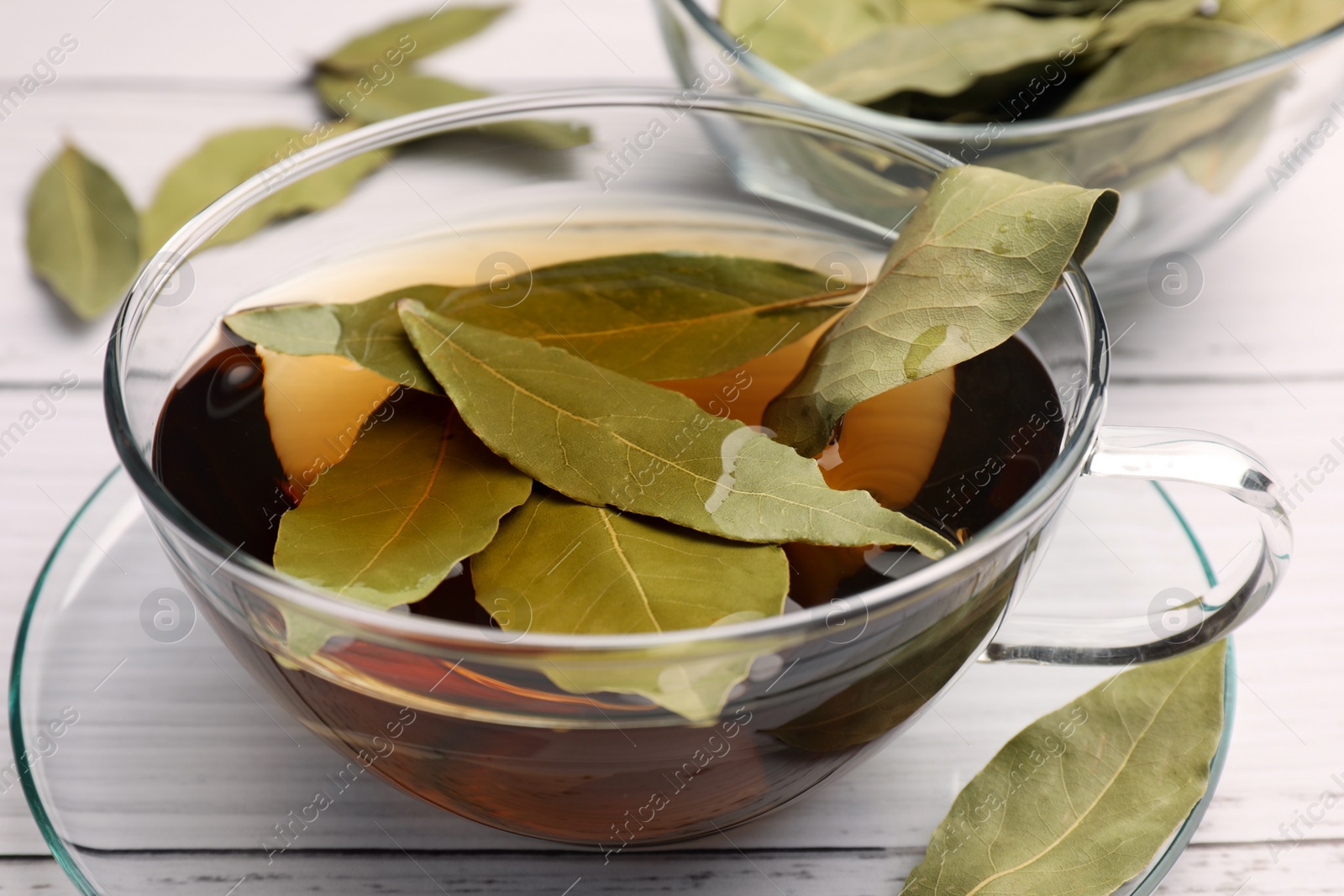 Photo of Cup of freshly brewed tea with bay leaves on white wooden table, closeup