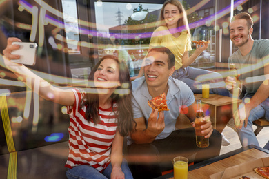 Image of Happy young people with delicious pizza taking selfie in cafe, bokeh effect