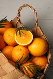Photo of Wicker basket with whole and cut ripe oranges on wooden background, closeup