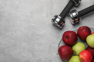 Photo of Healthy diet. Plate with apples and dumbbells on light grey textured table, flat lay. Space for text