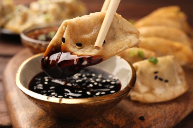 Photo of Taking delicious gyoza (asian dumpling) with soy sauce at table, closeup