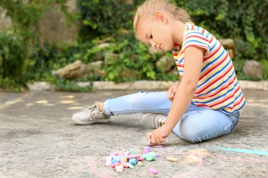 Upset little left-handed girl drawing with chalk on asphalt