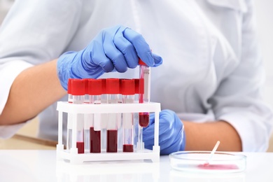 Scientist holding test tube with blood sample at table in laboratory