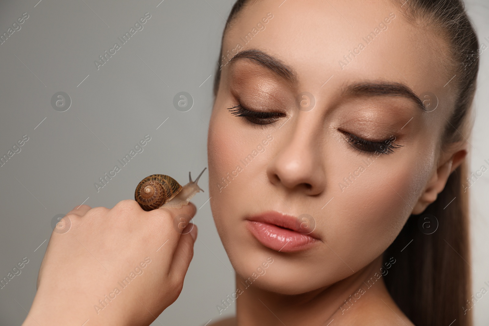 Photo of Beautiful young woman with snail on her hand against grey background, closeup