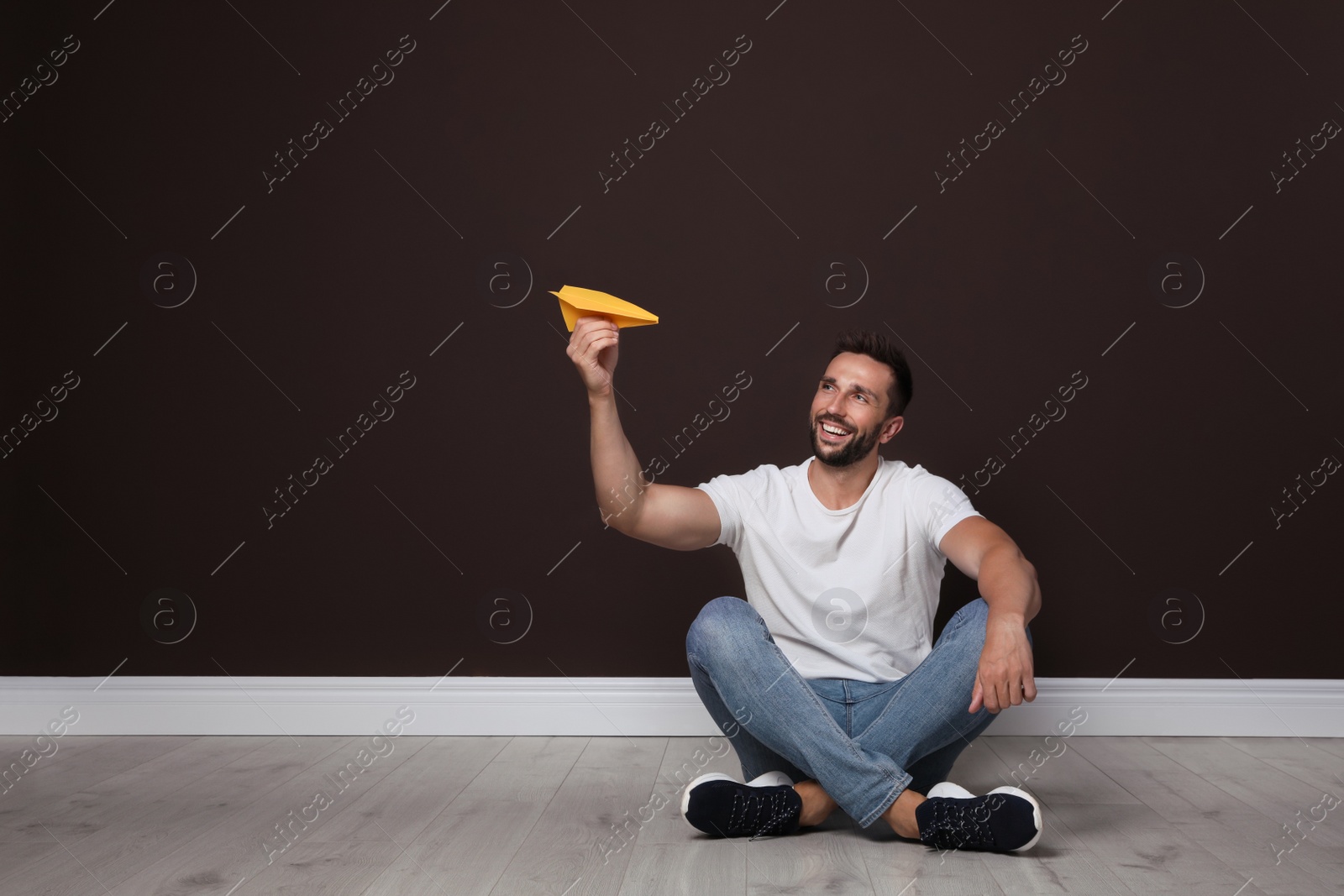 Photo of Handsome man playing with paper plane near brown wall. Space for text