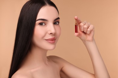 Photo of Beautiful young woman holding skincare ampoule on beige background