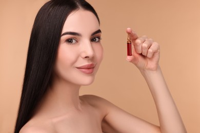 Beautiful young woman holding skincare ampoule on beige background