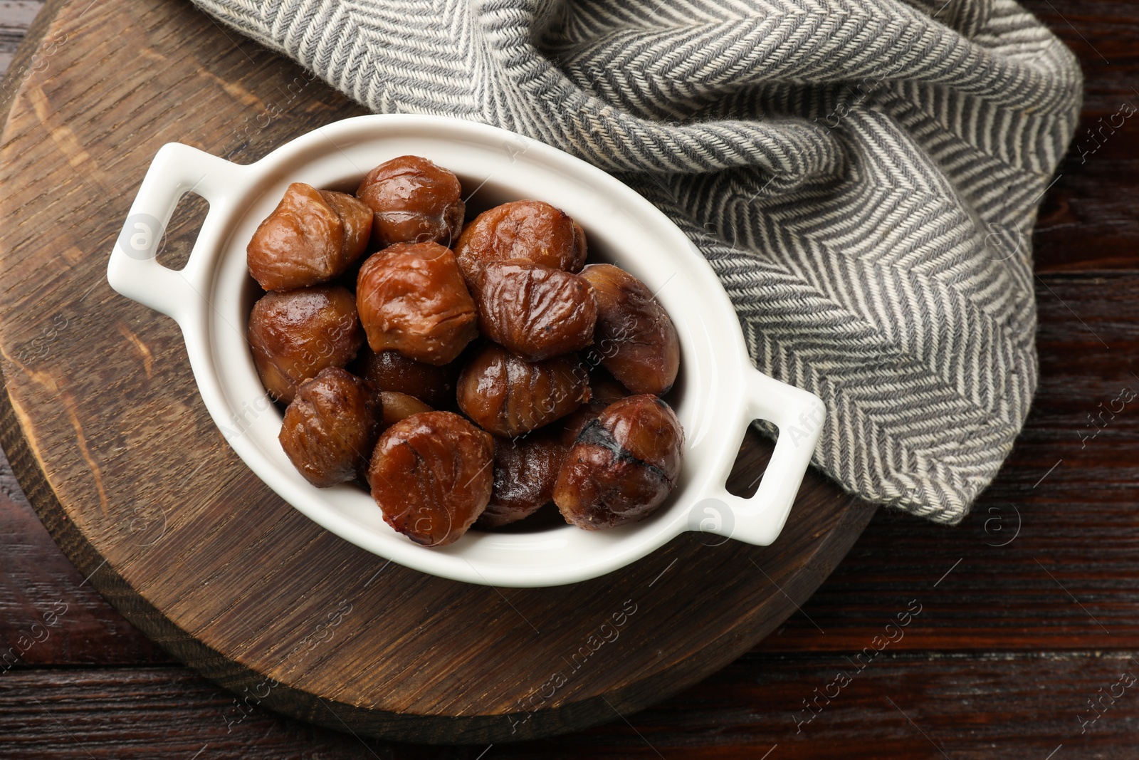 Photo of Roasted edible sweet chestnuts in dish on light wooden table, top view