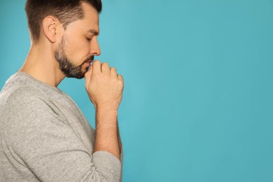 Photo of Man with clasped hands praying on turquoise background. Space for text
