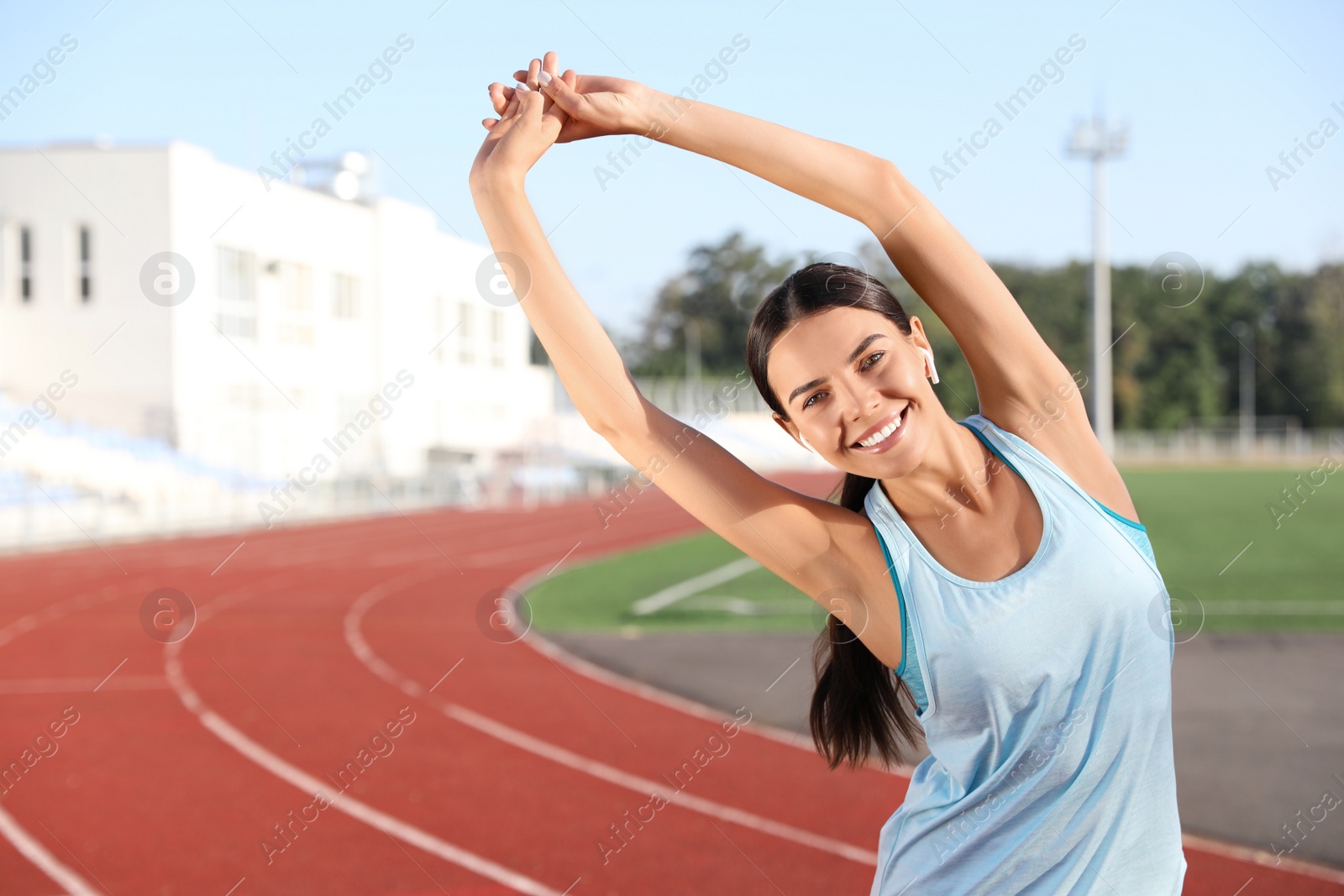 Photo of Young sportswoman with wireless earphones stretching at stadium