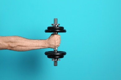 Photo of Male athlete holding metal dumbbell on color background. Space for text