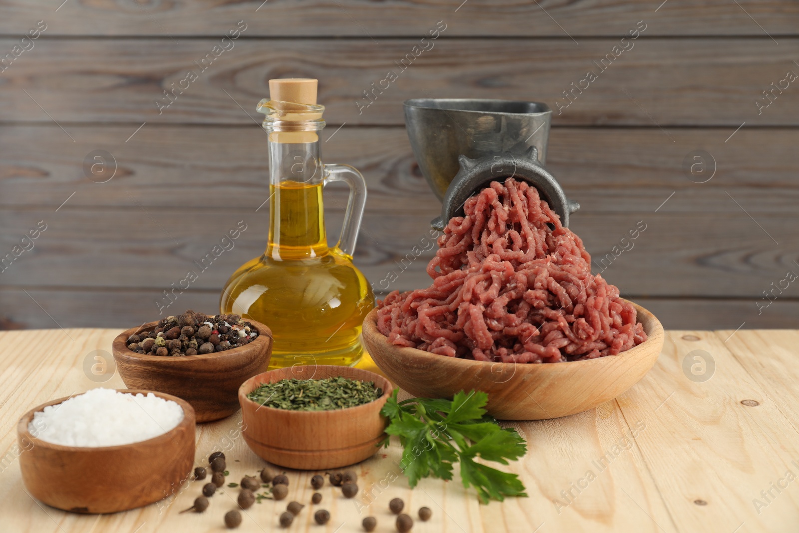 Photo of Mincing beef with manual meat grinder. Parsley, oil and spices on wooden table