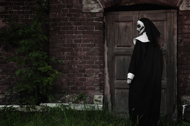 Photo of Scary devilish nun near wooden door outdoors, space for text. Halloween party look