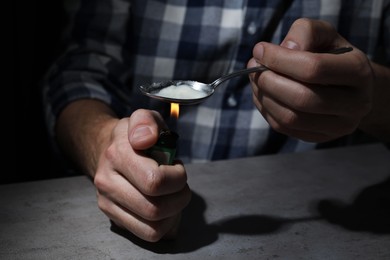 Photo of Man preparing drugs with spoon and lighter at grey table, closeup