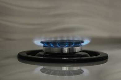 Gas burner with blue flame on modern stove, closeup. Space for text