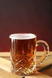Mug with fresh beer on wooden crate against color background