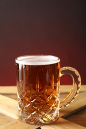 Photo of Mug with fresh beer on wooden crate against color background