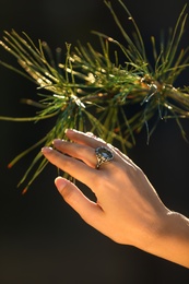 Young woman wearing beautiful silver ring with prehnite gemstone near pine, closeup