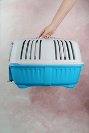 Photo of Woman holding light blue pet carrier against pink wall, closeup