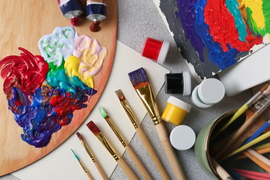 Artist's palette with mixed bright paints and brushes on textured table, flat lay