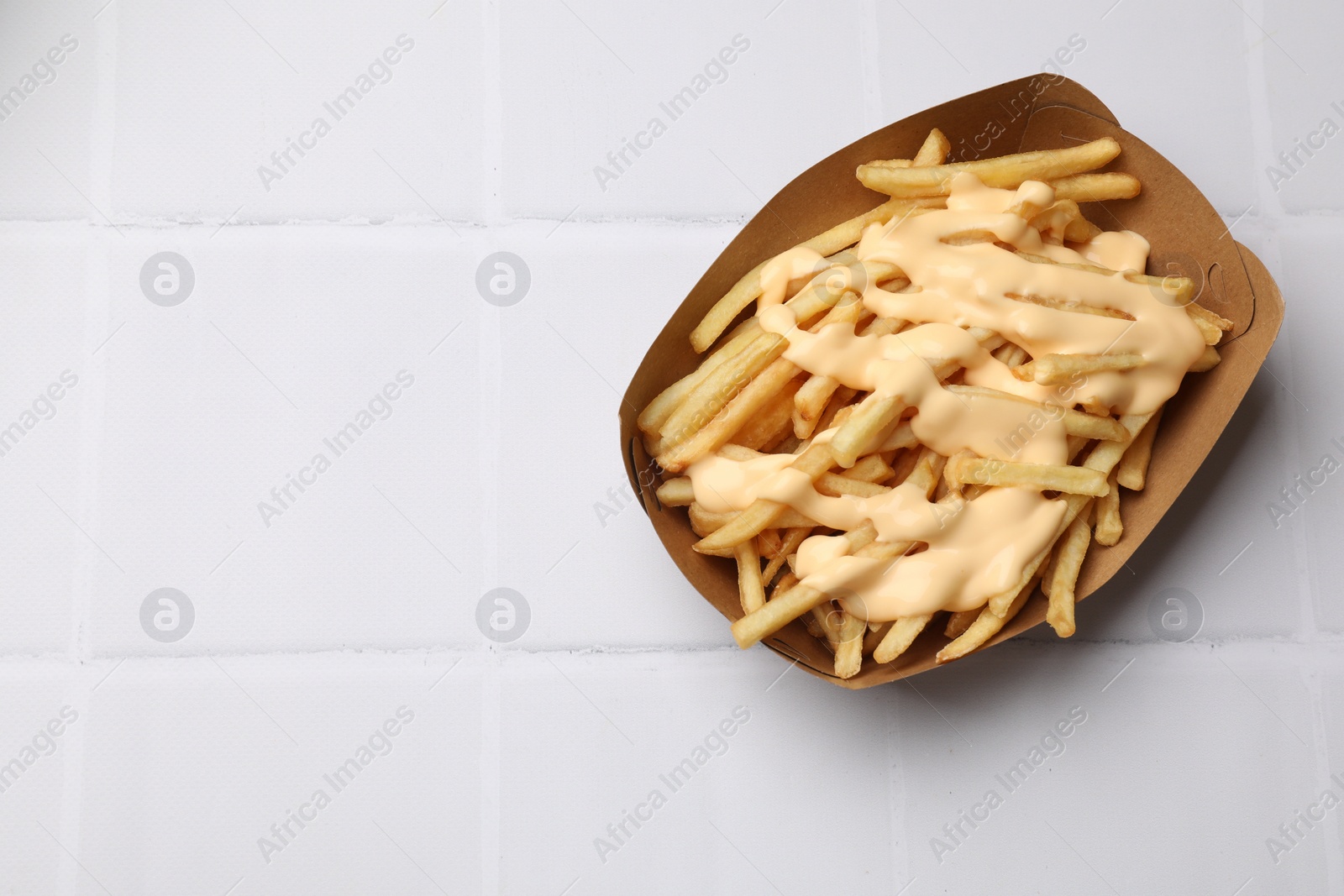 Photo of Delicious French fries with cheese sauce on white tiled table, top view. Space for text