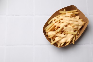 Delicious French fries with cheese sauce on white tiled table, top view. Space for text