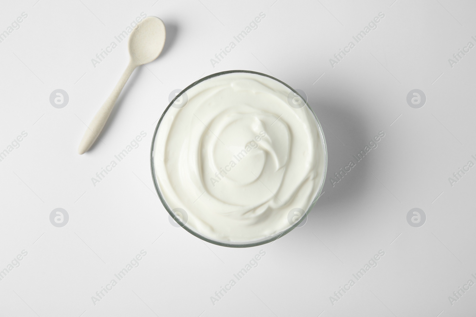 Photo of Glass bowl of sour cream and spoon on white background, top view