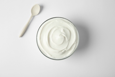 Photo of Glass bowl of sour cream and spoon on white background, top view