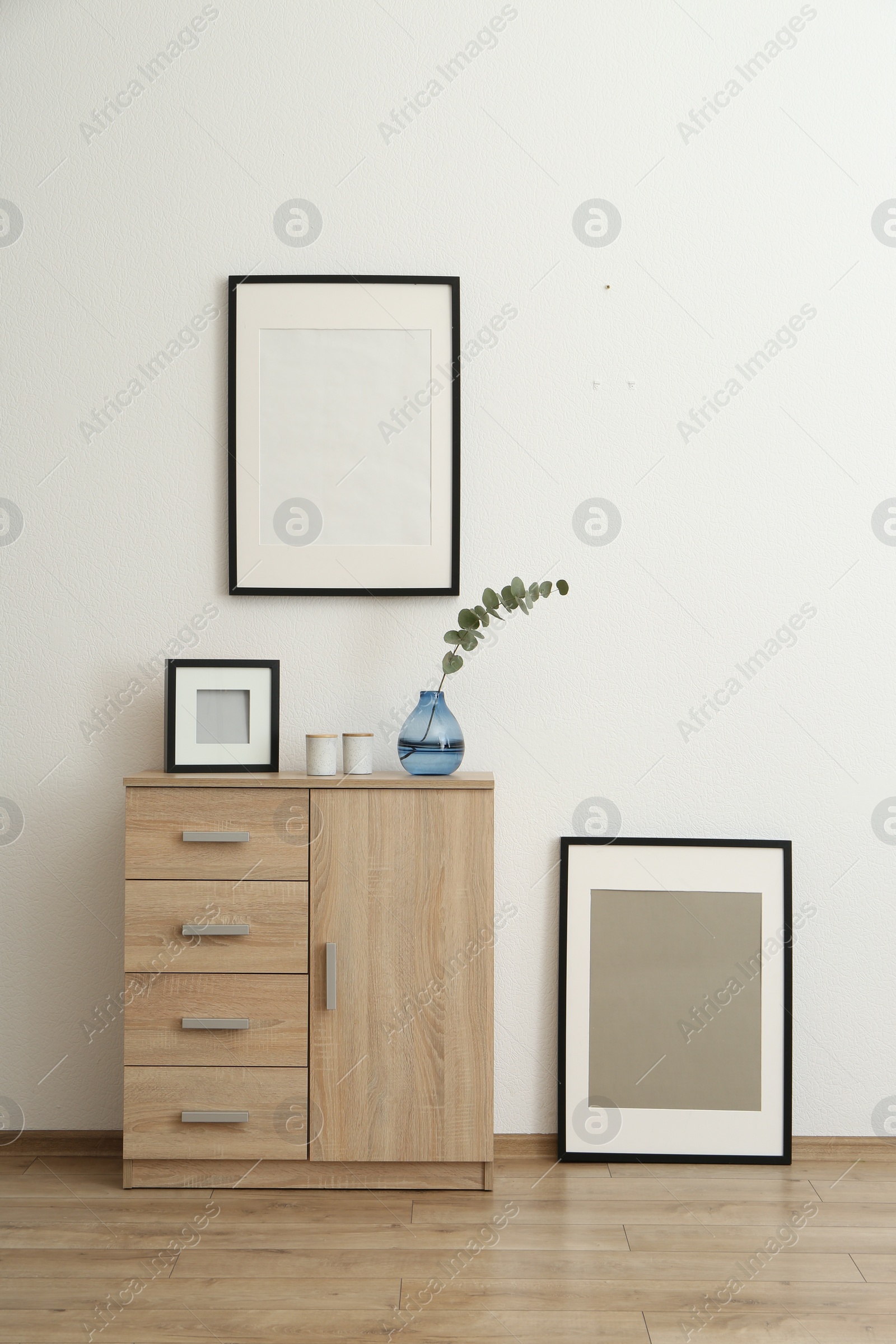 Photo of Wooden cabinet and photo frames in room with white wall. Interior design