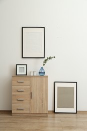 Photo of Wooden cabinet and photo frames in room with white wall. Interior design