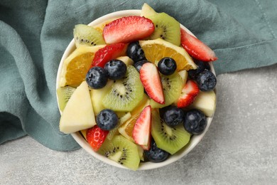 Photo of Tasty fruit salad in bowl on gray textured table, top view