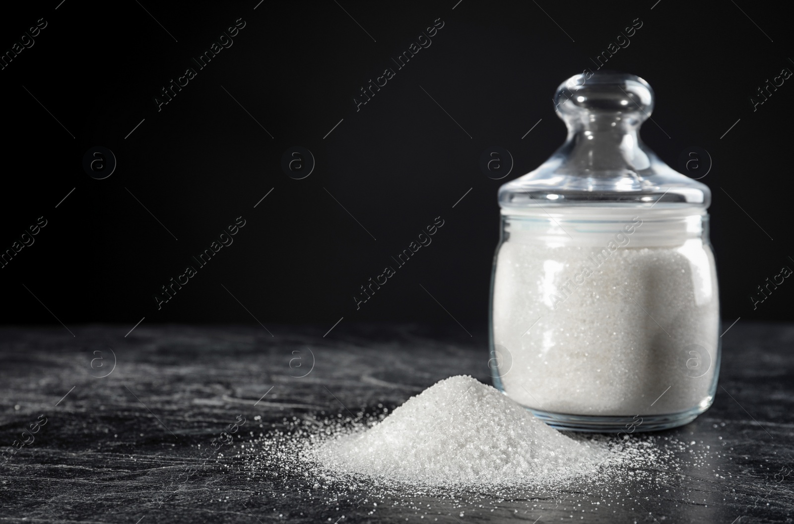 Photo of Bowl with granulated sugar on black table. Space for text