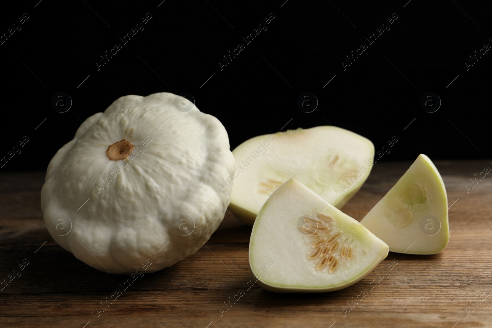 Photo of Whole and cut white pattypan squashes on wooden table against dark background