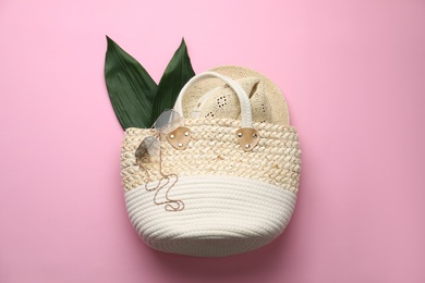 Photo of Elegant woman's straw bag with hat, tropical leaves and sunglasses on pink background, top view