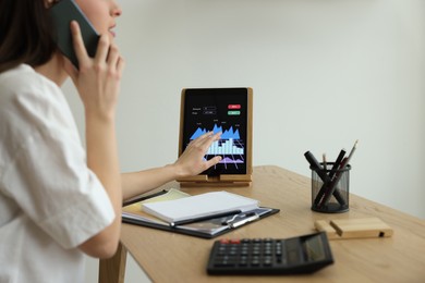 Photo of Businesswoman talking on phone while working with tablet in office, closeup. Forex trading