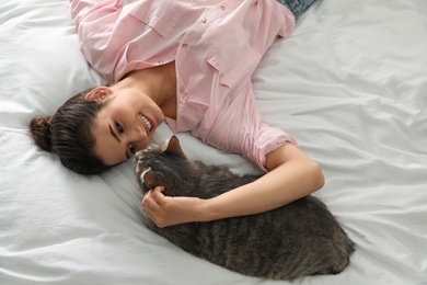 Photo of Young woman with cute cat on bed, above view. Pet and owner