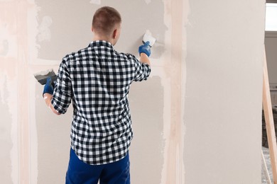 Photo of Man plastering wall with putty knife indoors, back view and space for text. Home renovation