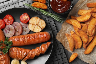 Delicious grilled sausages and vegetables on grey table, flat lay