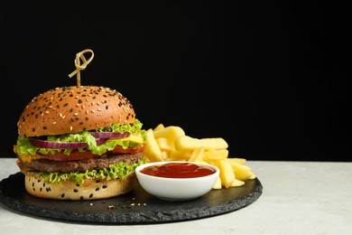 Photo of Burger with delicious patty, french fries and sauce on gray table against black background, space for text