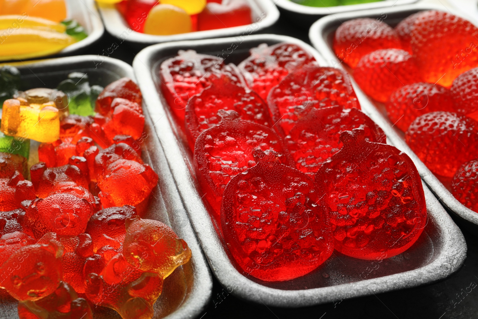 Photo of Different delicious gummy candies in containers, closeup